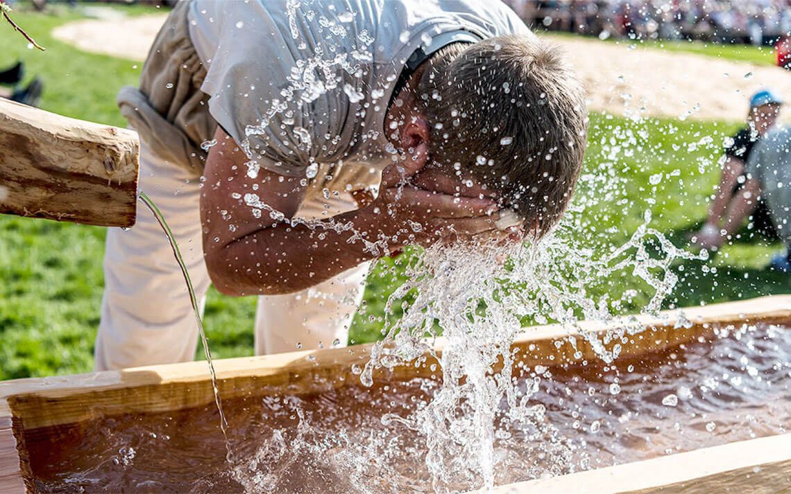 Schwinger mit weisser Schwingerhose am Brunnen und wäscht sich sein Kopf.